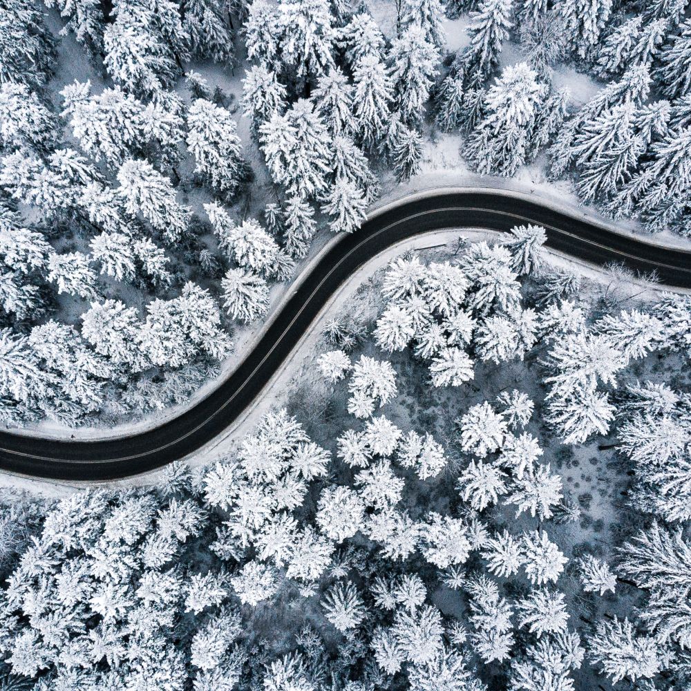 Curvy windy road in snow covered forest, top down aerial view