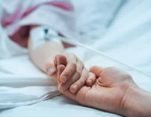 Recovering Little Child Lying in the Hospital Bed Sleeping, Mother Holds Her Hand Comforting. Focus on the Hands. Emotional Family Moment.